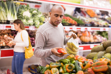 Buyer selects ripe bell peppers in the vegetable section of the supermarket