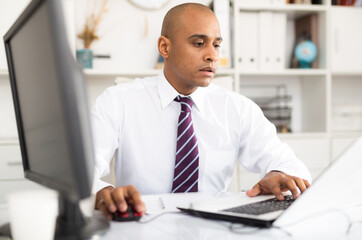 Adult businessman working in office with laptop, sitting at desk