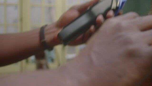 Close-up impersonal shot of hands of barber using hair clippers and comb for trimming neckline of male client