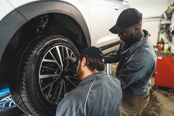 Fototapeta na wymiar Two men car mechanics at work, changing a car wheel of a lifted vehicle . High quality photo