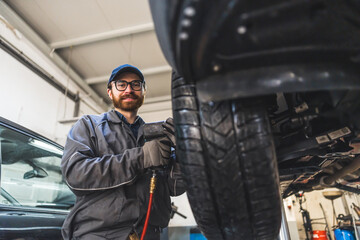 Car mechanic unscrewing car wheel of lifted automobile by pneumatic wrench at repair service station. High quality photo