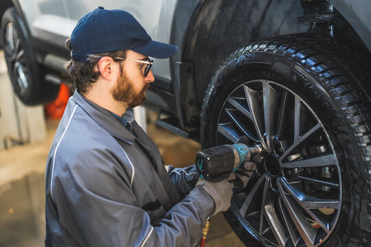 Mechanic with electric drill changing car tire on a lifted vehicle in repair shop. High quality photo