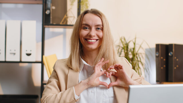 I love you. Young business woman makes symbol of love, showing heart sign to camera, express romantic feelings, express sincere positive feelings at home office workplace. Charity, gratitude, donation