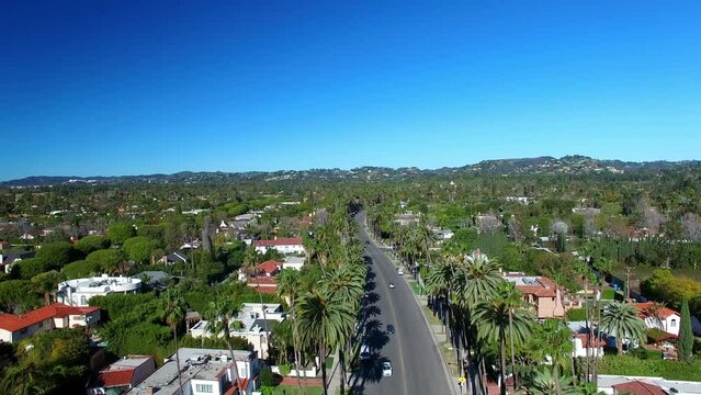 Aerial Shot Of Vehicles On Road Amidst Trees Against Sky, Drone Ascending Forward Over Houses In Suburb On Sunny Day - Beverly Hills, California