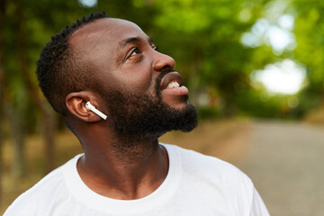 Happy young adult african american man walking in the park wearing headphones