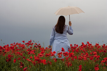 mujer con paraguas blanco en campo de amapolas con vestido azul en día nublado