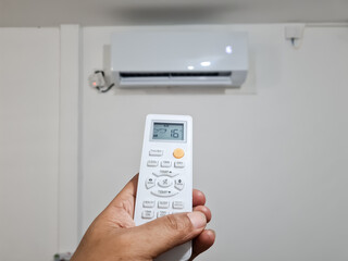 male hand holding ac remote and adjusting air conditioner temperature by using remote control.