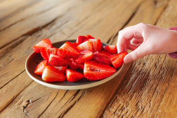  eating strawberries.Hands take chopped delicious strawberries from a plate on a wooden...