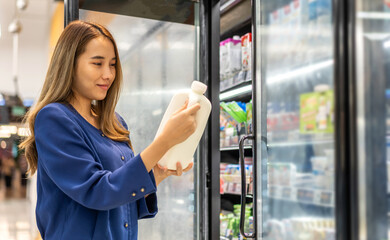 Portrait of beauty asian happy woman relax and enjoy shopping time with trolley cart buy healthy food fresh dairy product of milk and cheese in commercial refrigerators at shopping supermarket