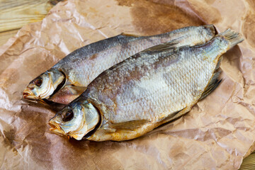 On table covered with paper is glass of beer and appetizer - dried jerked bream, whole fish