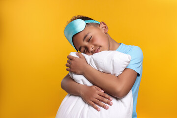 Boy with pillow and sleep mask on yellow background. Insomnia problem