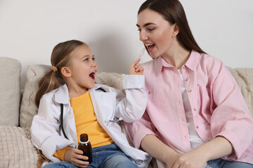 Little girl playing doctor with her mother at home