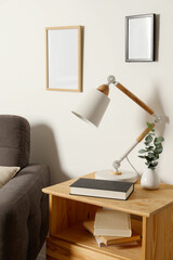 Stylish modern desk lamp, book and plant on wooden cabinet near white wall indoors