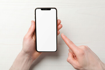 Man holding smartphone with blank screen at white wooden table, top view. Mockup for design