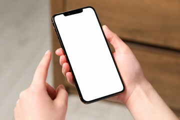 Woman holding smartphone with blank screen indoors, closeup. Mockup for design