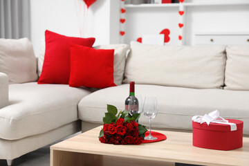 Beautiful rose flowers, gift box, glasses and bottle of wine on coffee table in cozy living room decorated for Valentine Day. Interior design
