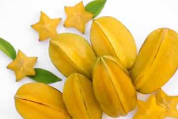 Delicious cut and whole carambolas with green leaves on white background, above view