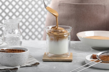 Woman making dalgona coffee at light gray table, closeup