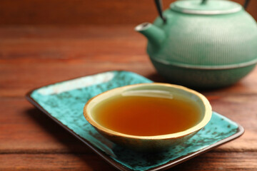 Teapot and cup of freshly brewed tea on wooden table, closeup. Traditional ceremony