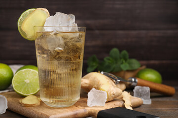 Glass of tasty ginger ale with ice cubes and ingredients on wooden table, space for text