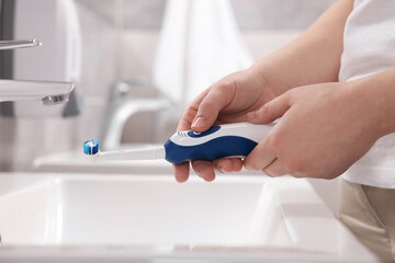 Fototapeta premium Woman holding electric toothbrush above sink in bathroom, closeup