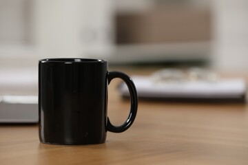 Black ceramic mug on wooden table at workplace. Space for text