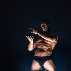 Muscular athlete in an epic pose, dark background, bright light from below, the concept of sports and bodybuilding