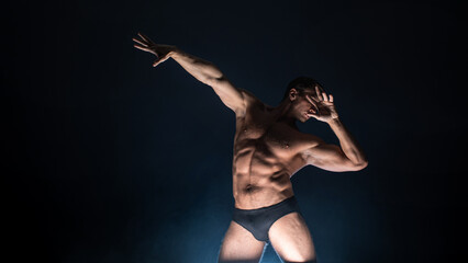 Muscular athlete in an epic pose, dark background, bright light from below, the concept of sports and bodybuilding