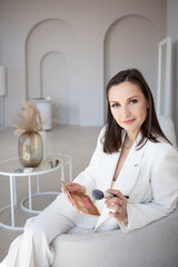 Fashion and beauty, stylish makeup artist in a white jacket with makeup brushes in her hands, business portrait of a makeup artist stylist or director of a beauty studio