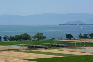 Fototapeta premium 初夏の琵琶湖を背景に走る223系普通列車 （北陸本線 田村 - 長浜, 2023年6月）