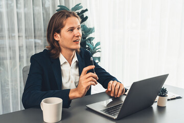 Businessman in black suit working on laptop at his workspace desk. Smart executive researching financial data and planning marketing strategy on corporate laptop at modern workplace. Entity