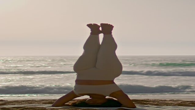 Vertical woman headstand yoga pose on seashore at sunrise. Girl training balance