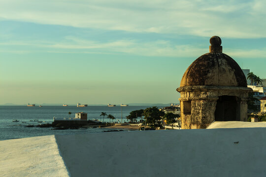vis&atilde;o do forte de santa maria a parte do farol da barra, com a baia de todos os santos e navios cargueiros ao fundo durante o por do sol. Sentinela e muro do farol da barra comp&otilde;em a moldura da imagem