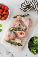 Raw chicken legs with spices and rosemary sprigs on a wooden cutting board.
