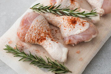 Raw chicken legs with spices and rosemary sprigs on a wooden cutting board.