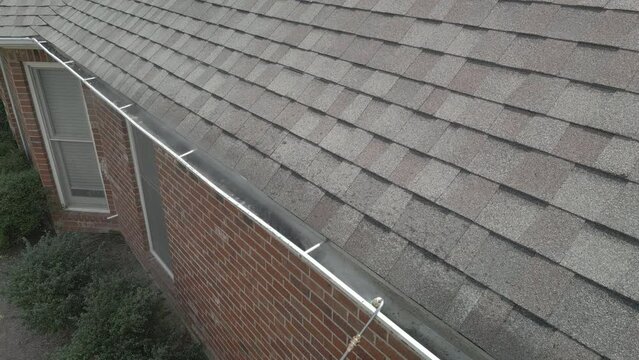 Cleaning dirty, metal gutters on a home using a pressure washer with long extension wand.