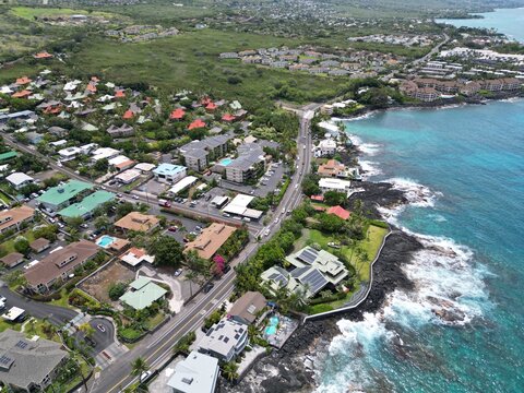 View of coastal Kailua-Kona on the Big Island of Hawai'i. Aerial drone shot along the coast with palm trees, Condominiums, coastal highway, and blue and green waters with volcanic rock.