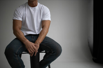 handsome male actor model posing sitting on armchair in studio in white t-shirt.