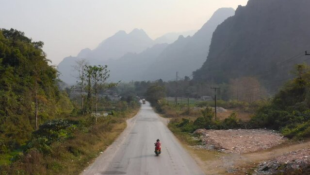 Overtake Shot Of Biker Riding Motorcycle On Rural road, Vang Vieng Village, Thailand