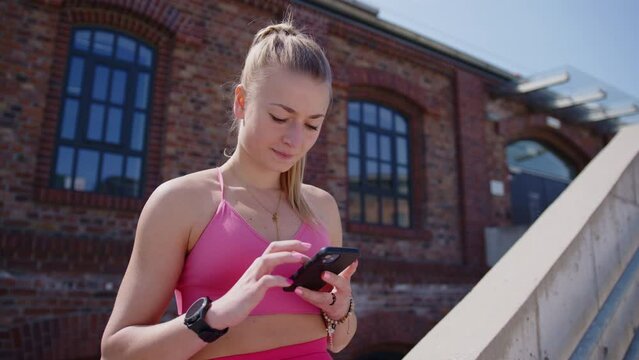 Young caucasian woman in sportswear uses phone and smartwatch, closeup