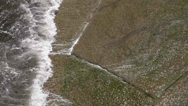 Close up of waves crashing on the boat ramp and causing small riptide with sea water flowing bac k under the new waves on stone shore