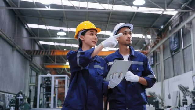 Smart engineer worker man and woman in uniform safety and wear helmet consulting and using tablet help analyze data in warehouse at manufactory.Industrial and factory warehouse concept