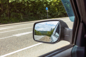 The view in the rearview mirror while driving down the road in the woods.