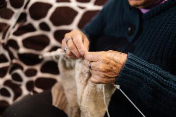 Mujer latina, adulto mayor , feliz y concentrada, en la sala de casa usando unos palitos de tejer y...