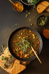 Healthy vegetarian lunches, brown lentil soup with tomatoes and carrots, potatoes and curry spices, toasted croutons, bowl with soup on cutting board on brown background