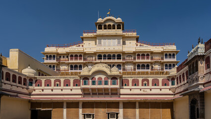 Facade of the ancient City Palace, Jaipur. Multi-storey sandstone building with galleries, colonnades, balconies, domes, spires. Blue sky. India.