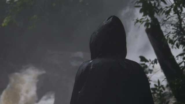 Person in the raincoat against the water element. Waterfall. Storm. Heavy rain.