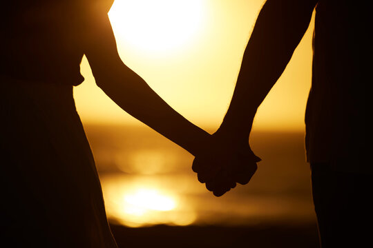 Holding hands, couple and silhouette on beach at sunset for vacation or holiday outdoor. Behind man and woman in nature with peace, calm and ocean for love, creative shadow and travel or freedom