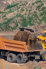 Loader pours earth into the dump truck body on a summer day