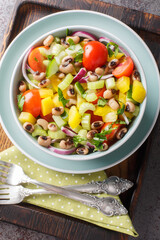 Fresh black-eyed pea salad with tomatoes, celery, pepper, cucumber and onion close-up in a bowl on the table. Vertical top view from above